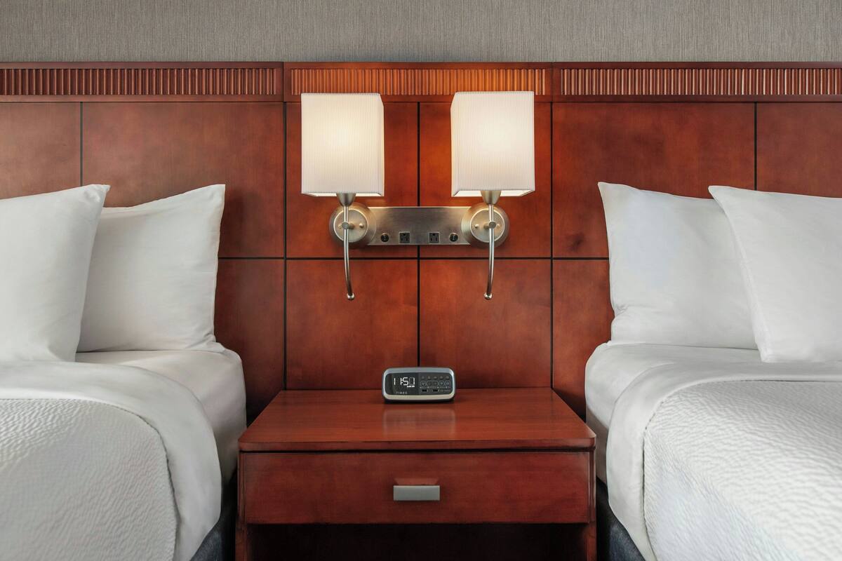 Ein Hotelzimmer mit einem hölzernen Kopfteil, zwei Nachttischlampen, einer digitalen Uhr und einem kleinen Nachttisch.
