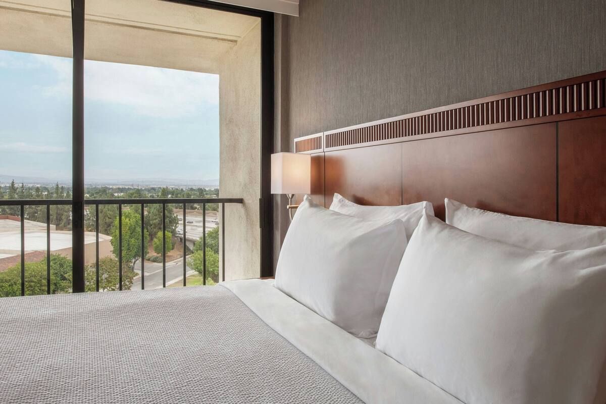 Ein Hotelzimmer mit einem großen Bett, Stadtblick und einem Balkon mit Geländer.