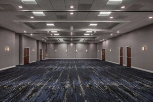 A large conference room with a dark patterned carpet, recessed lighting, and multiple doors along the walls.