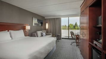 Habitación de hotel con una cama grande, un escritorio, una silla, un televisor y un balcón con vistas a árboles.