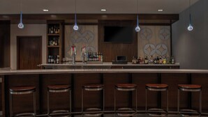 Un espace bar avec un comptoir en bois, des tabourets de bar et un téléviseur fixé au mur.