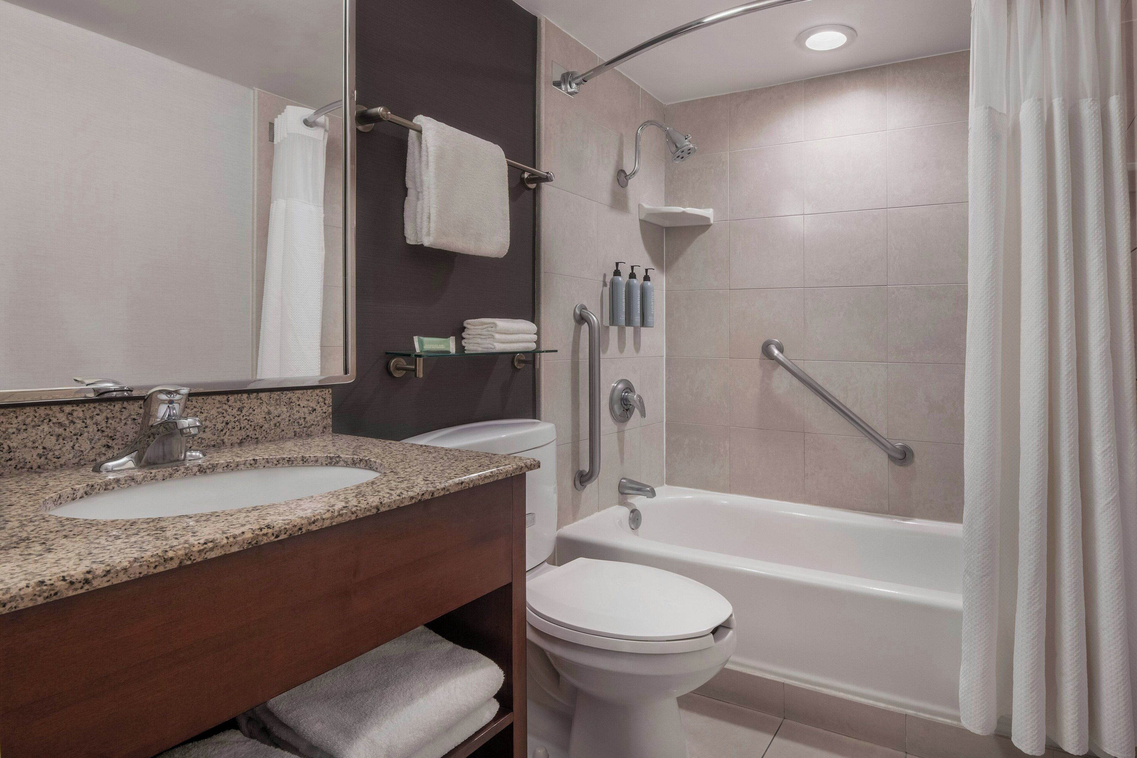 Un baño moderno con lavamanos de granito, inodoro y ducha a ras de suelo con barra de apoyo.