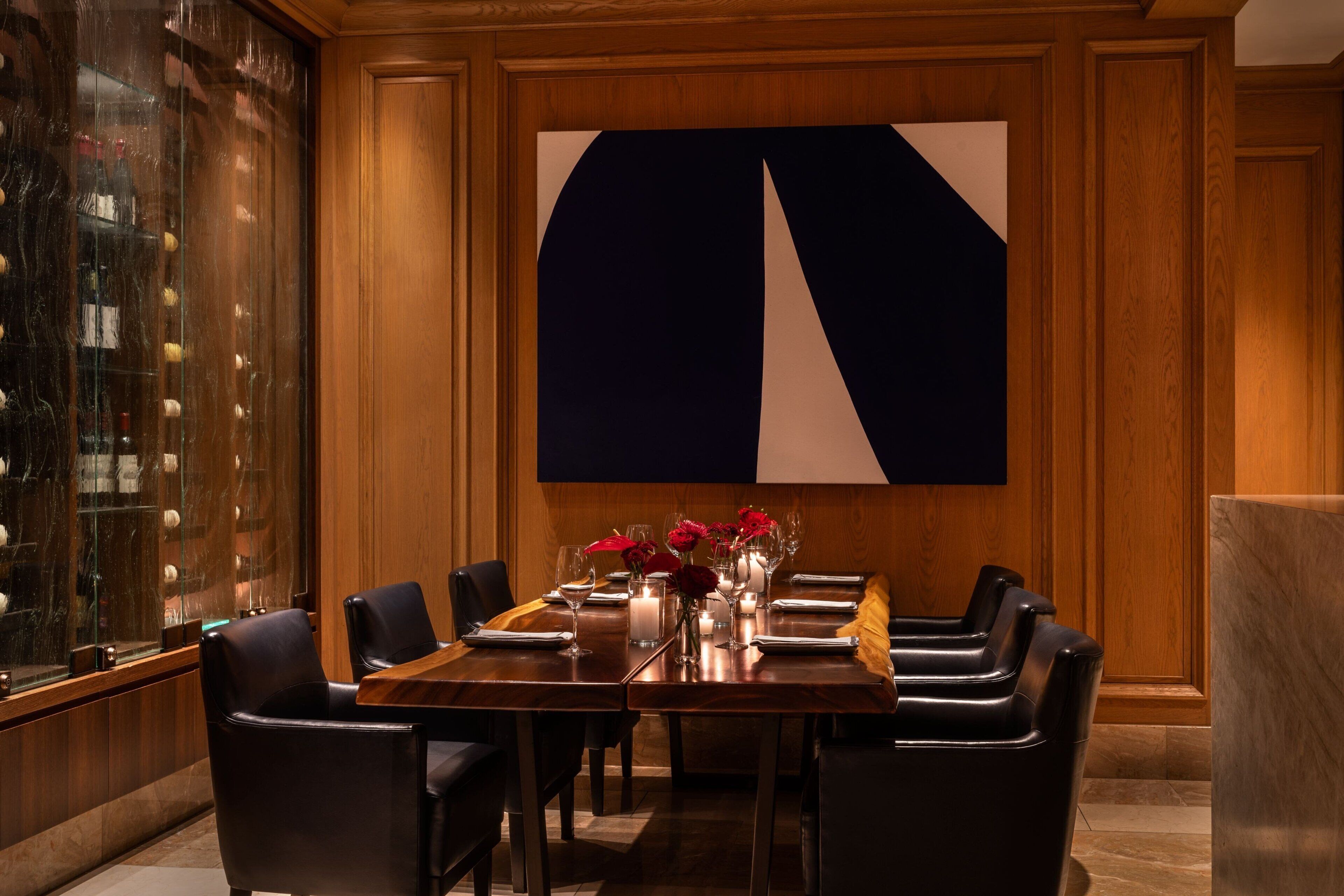 A dining area with a wooden table, black chairs, and a large abstract painting on the wall.