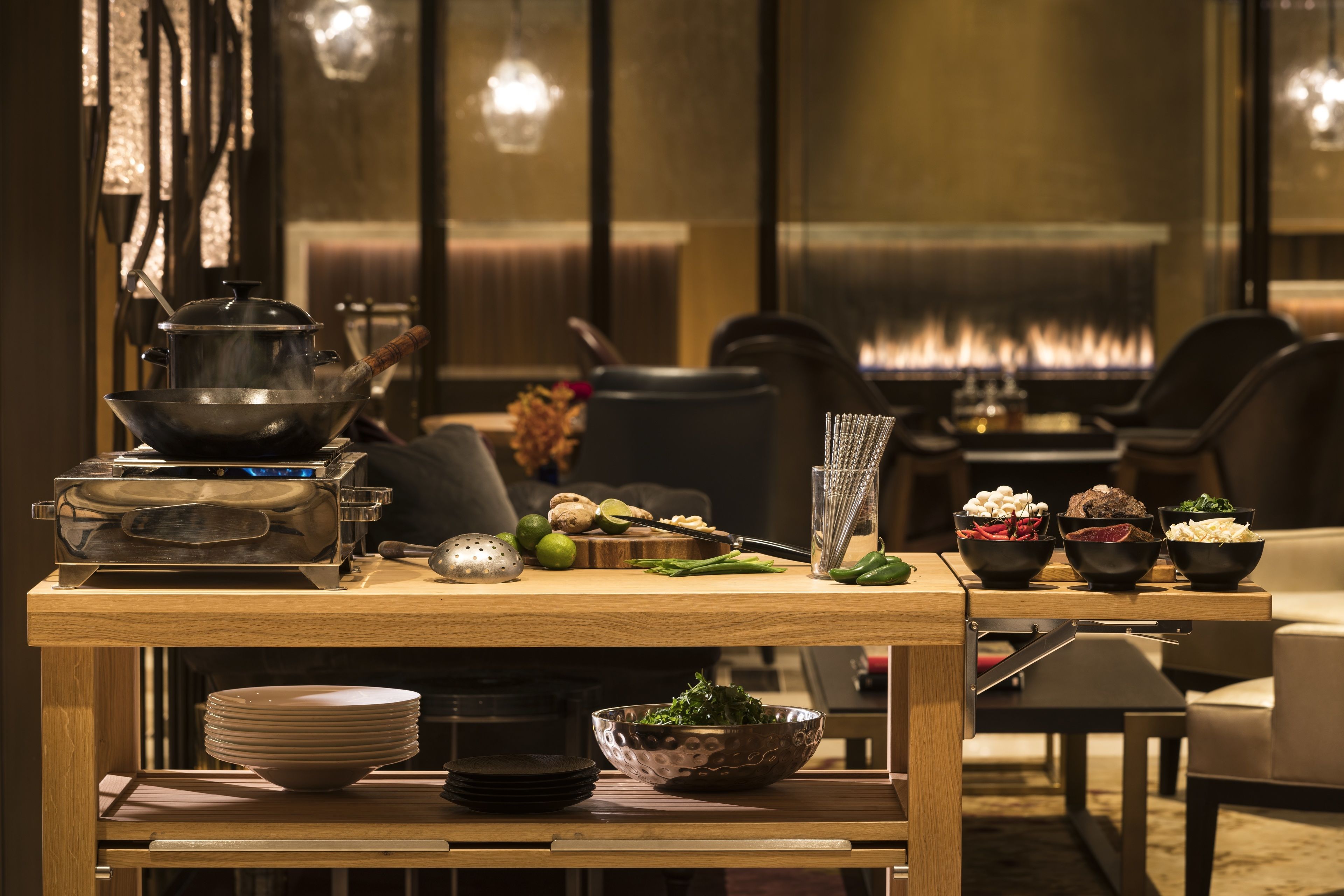 A dining area with a wooden table set with plates, bowls, and a pot on a portable stove.