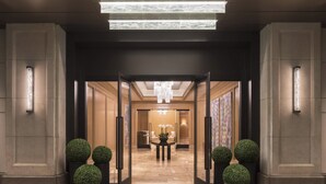 A hotel entrance with a glass door, a reception desk, and a chandelier.