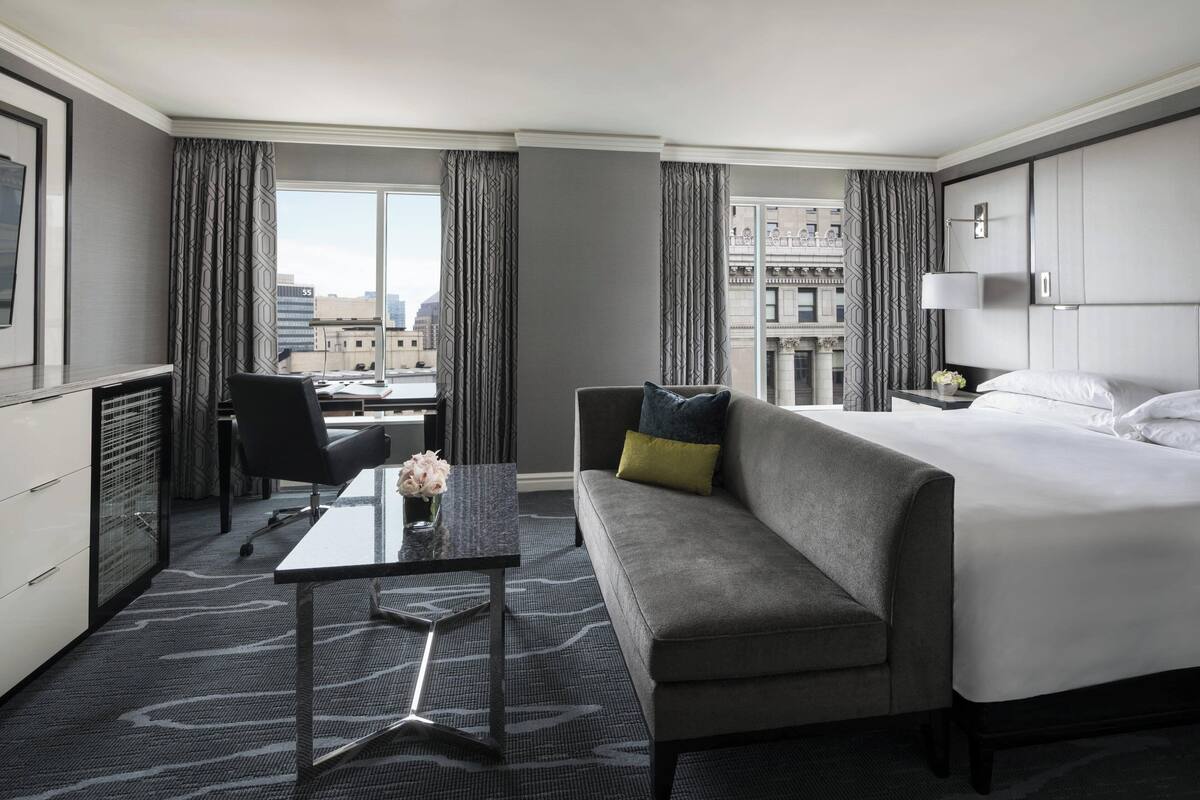 A hotel room with a large bed, a sofa, a desk, and a view of the city.