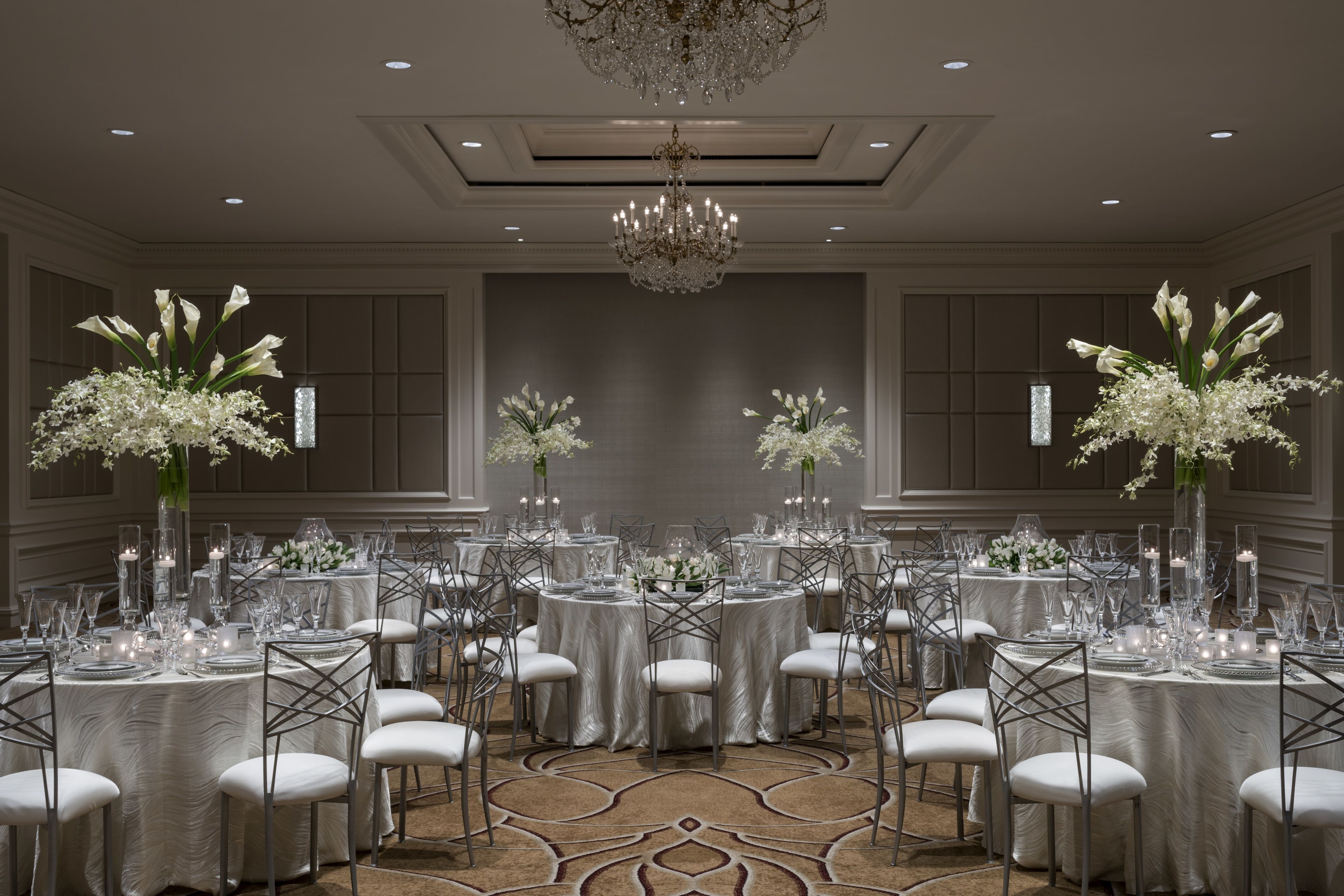 A formal dining room with round tables, white chairs, and floral centerpieces.
