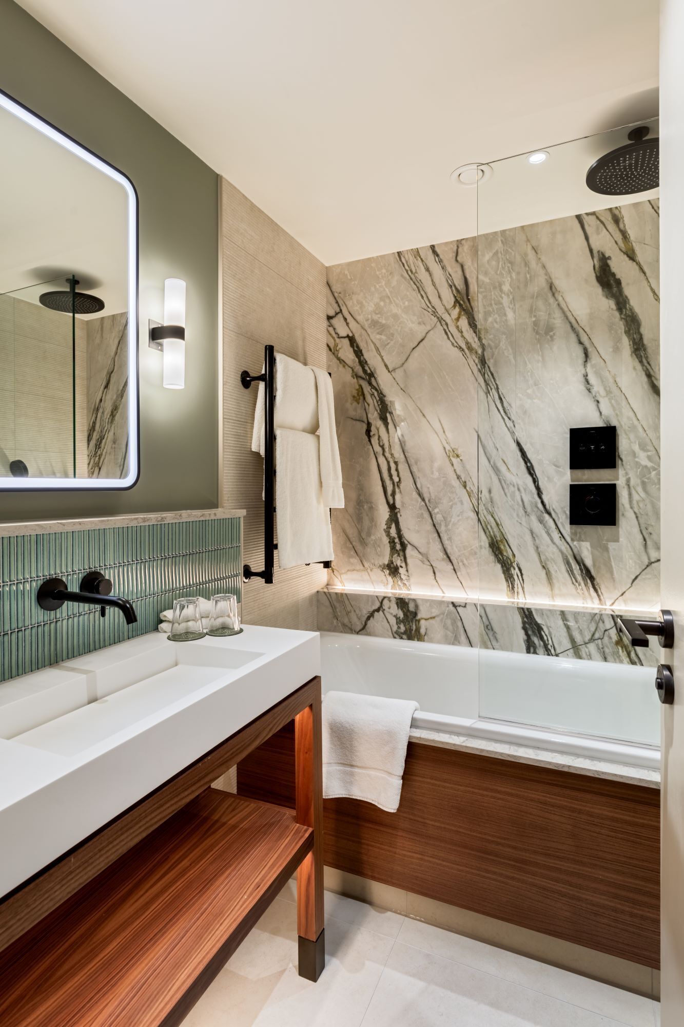 Un baño moderno con pared de mármol, un espejo grande, tocador de madera, bañera y ducha.