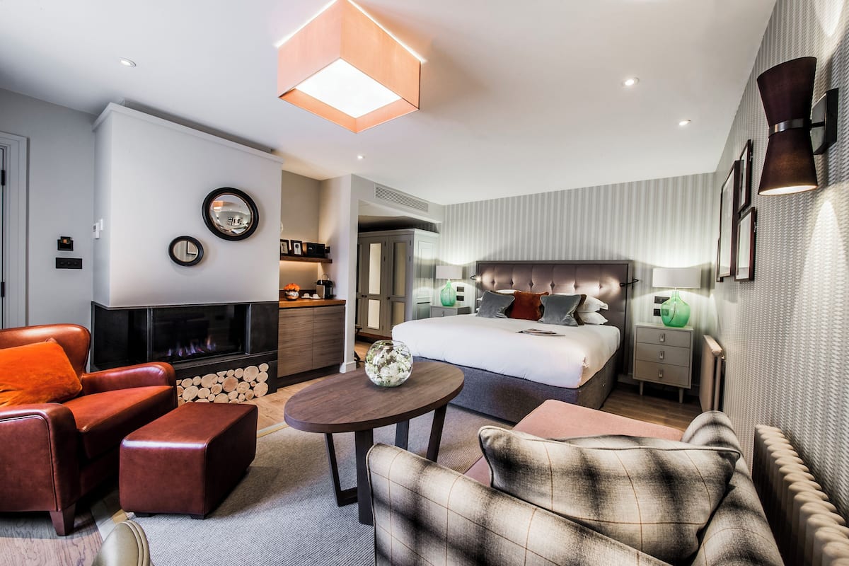 Ein modernes Hotelzimmer mit einem großen Bett, einem Kamin, einer Couch und einer Essecke.