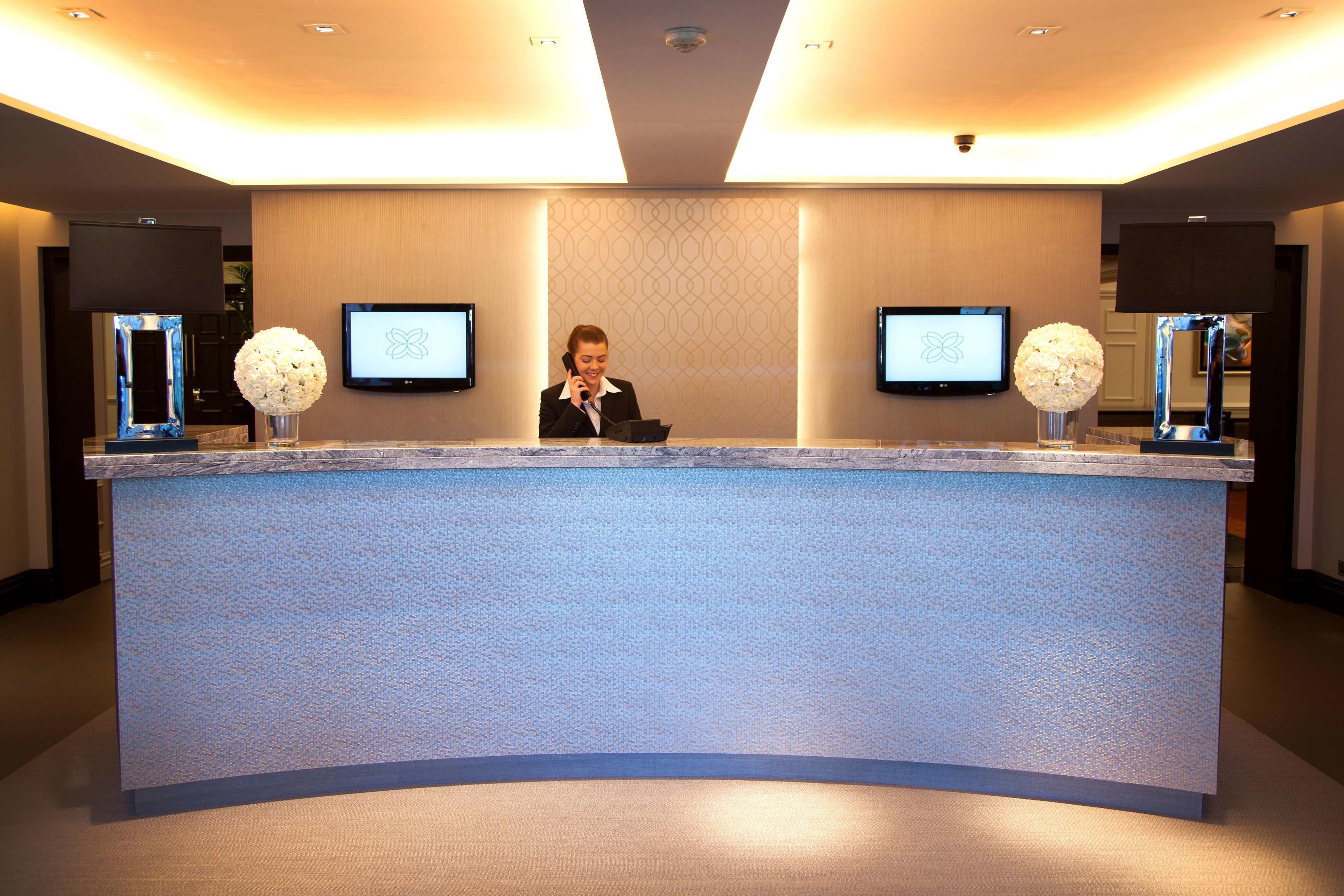 A reception desk with two monitors, a receptionist, and two decorative vases.