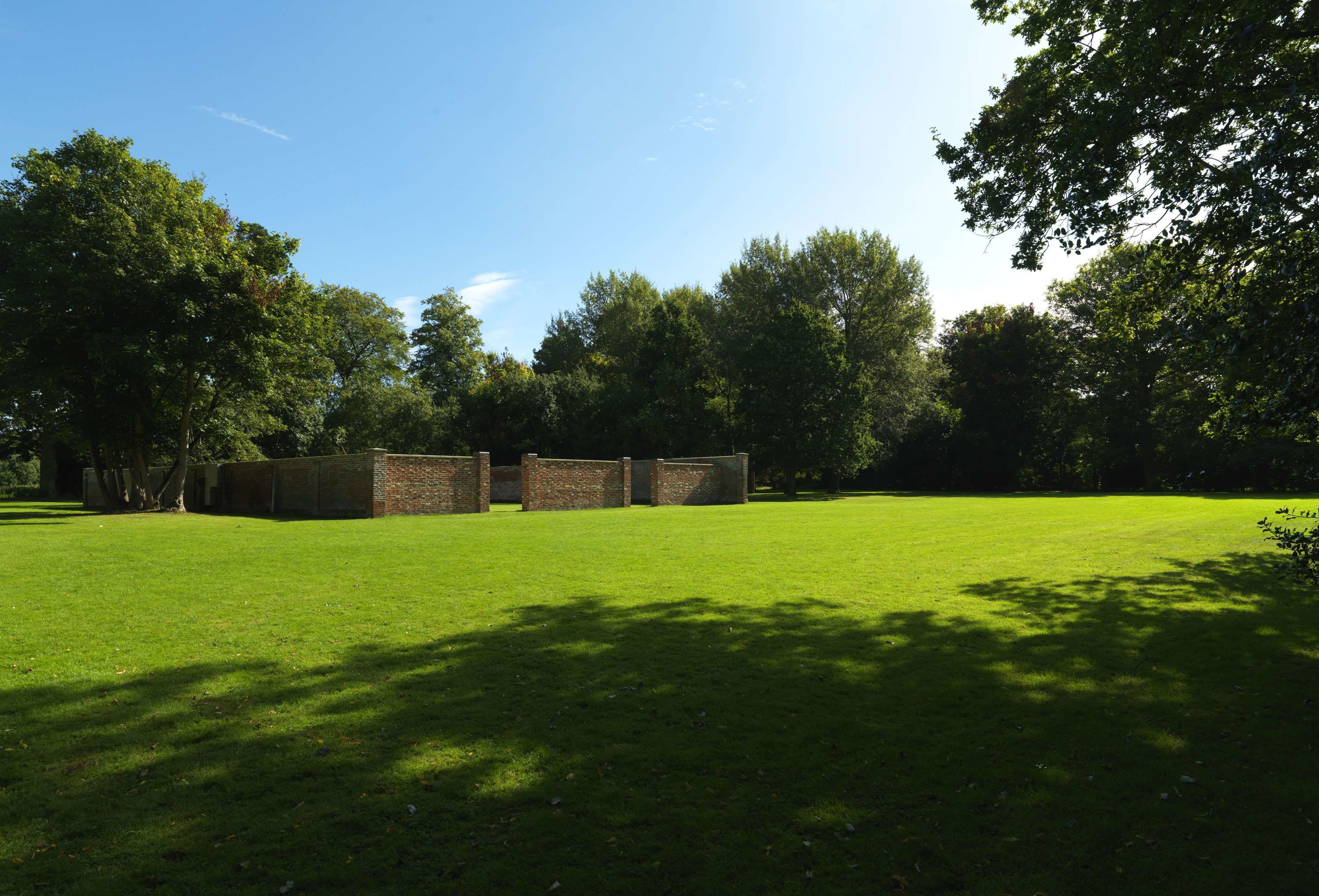 A grassy area with brick structures, trees, and a clear sky.