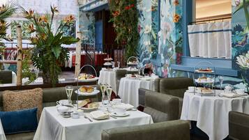 A restaurant with tables set for a tea service, featuring floral wall art and comfortable seating.