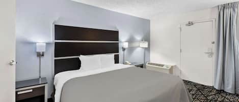 A hotel room with a large bed, bedside tables with lamps, a wall-mounted heater, and a door with curtains.