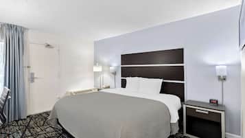 A hotel room with a large bed, a bedside table with a lamp, a nightstand with a clock, and a door with a curtain.