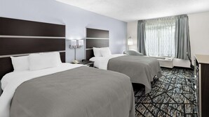 Quarto de hotel com duas camas, uma escrivaninha, uma cadeira e uma janela grande com cortinas.