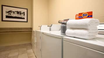 A laundry area with stacked white towels, a Tide detergent box, and a framed picture on the wall.