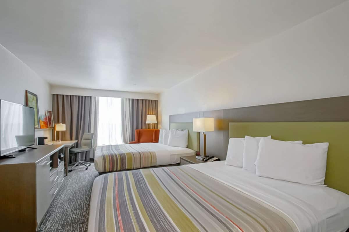 A hotel room with two beds, a desk with a chair, a television, and a window with curtains.