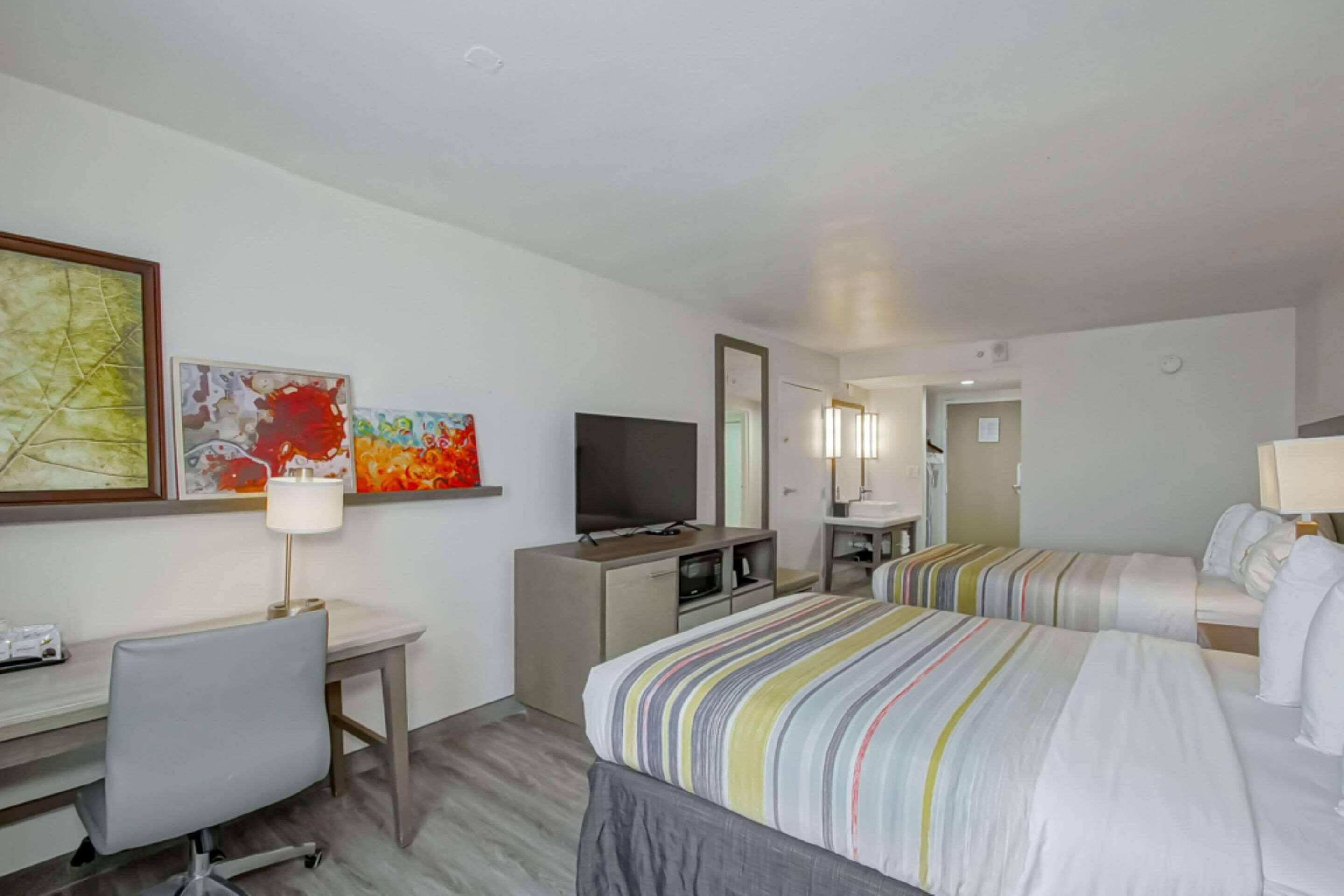 Ein Hotelzimmer mit Schreibtisch, Fernseher, zwei Betten und Bildern an den Wänden.
