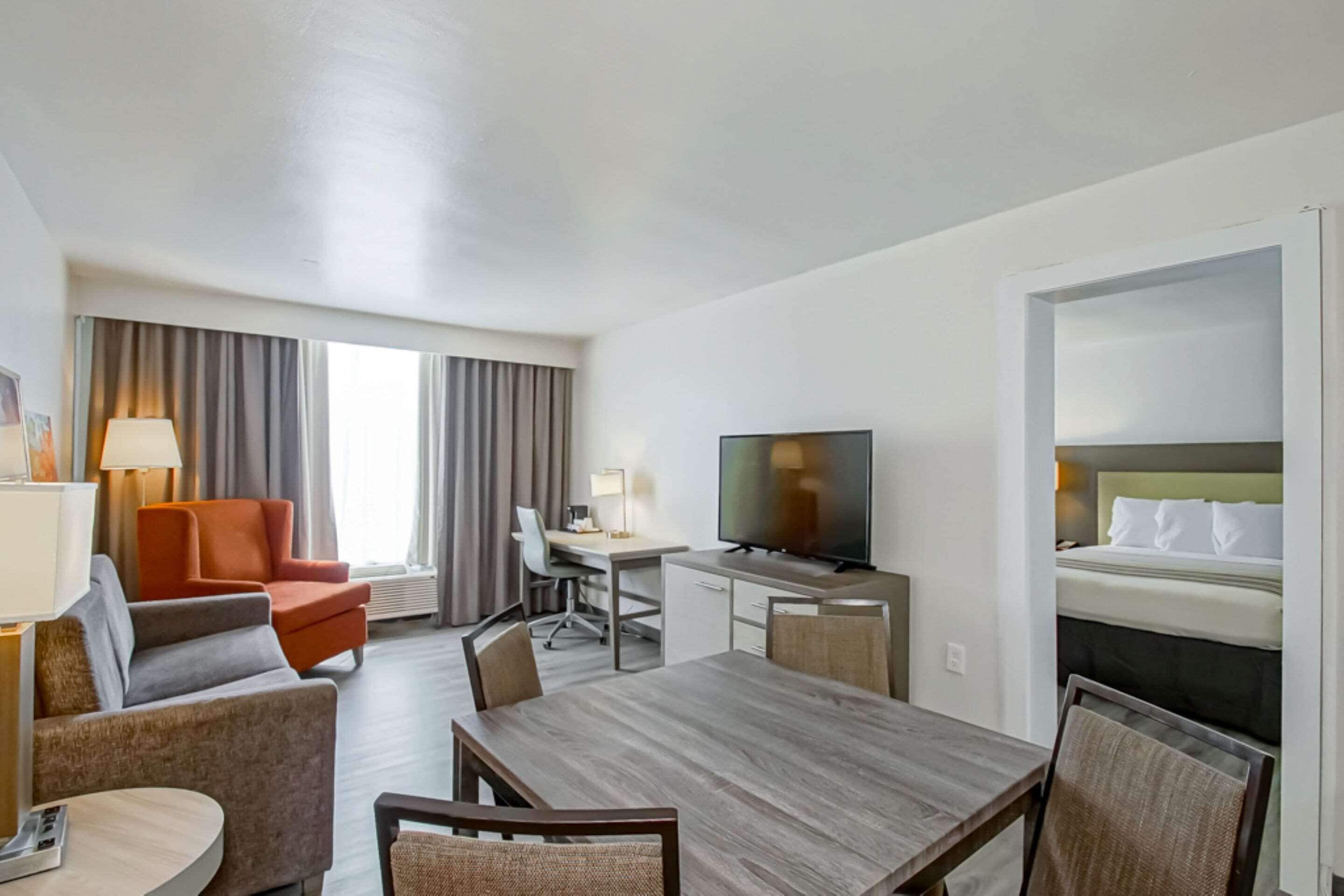 A hotel room with a wooden dining table, a TV, a sofa, a desk, and a bed.