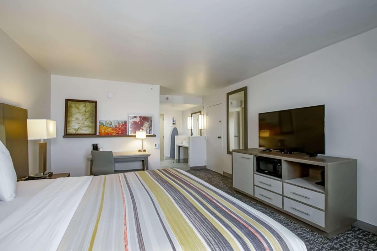 A hotel room with a bed, a desk, a TV, and a mirror.