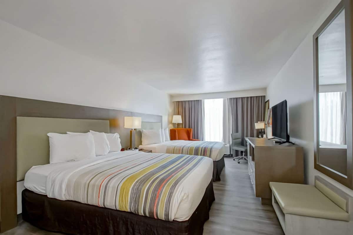 A hotel room with two beds, a desk, a TV, and a large window.