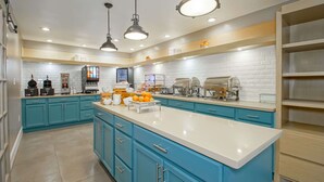 A modern kitchen with teal cabinetry, white countertops, and pendant lighting. - Country Inn & Suites by Radisson, New Orleans I-10 East, LA (New Orleans)