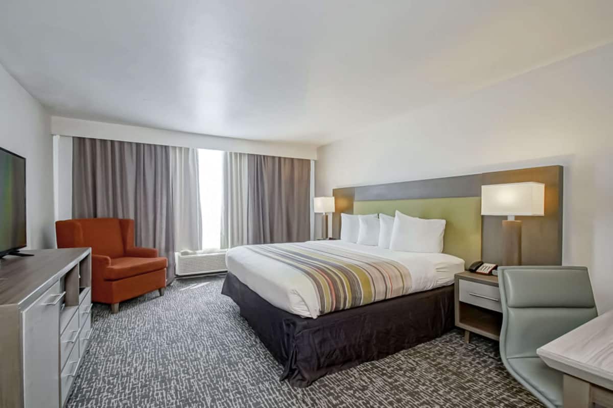 A hotel room with a large bed, two chairs, a desk, and a TV.
