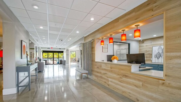 A modern reception area with a wooden reception desk, a bench, and a view of the lobby. - Country Inn & Suites by Radisson, New Orleans I-10 East, LA (New Orleans)