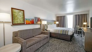 A hotel room with a bed, a sofa, a desk, and two lamps. - Country Inn & Suites by Radisson, New Orleans I-10 East, LA (New Orleans)