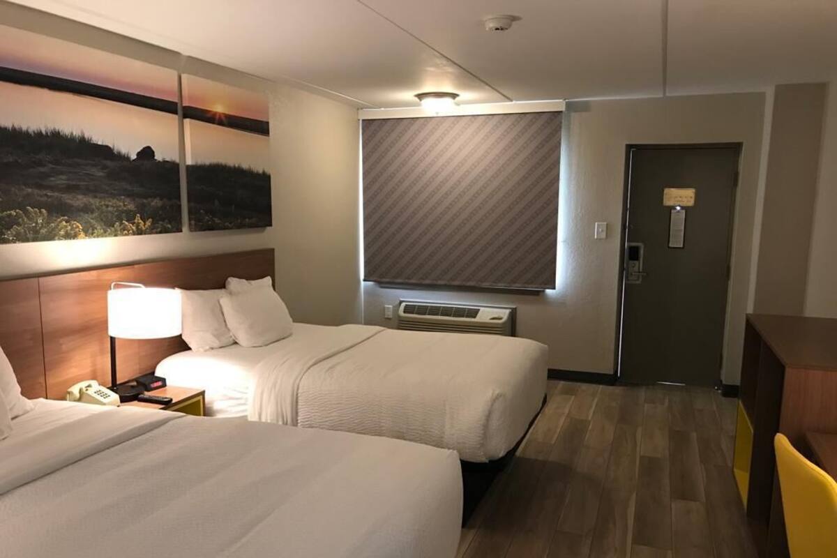 A hotel room with two beds, a nightstand with a phone, a wall-mounted air conditioner, and a door with a sign.