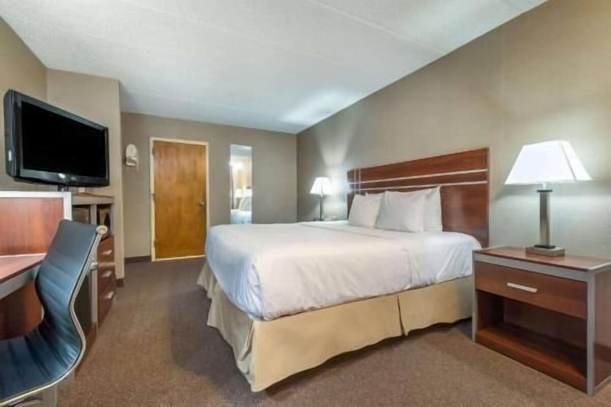 A hotel room with a bed, a desk, a chair, a television, and a door.
