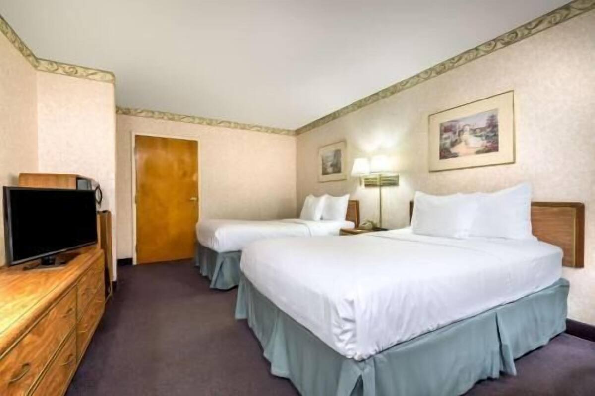 A hotel room with two beds, a TV, a dresser, and a door.