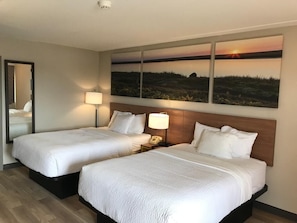 A hotel room with two beds, a large painting of a sunset, and a mirror on the wall. - Days Inn by Wyndham Vineland (Vineland)