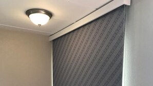 Ein Zimmer mit einem gemusterten Fensterladen, einer Wand-Klimaanlage und einem Holzboden.