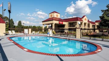 A swimming pool with a red border, surrounded by a fence, and a building with a red roof and a sign that reads 'Red Roof Inn.'