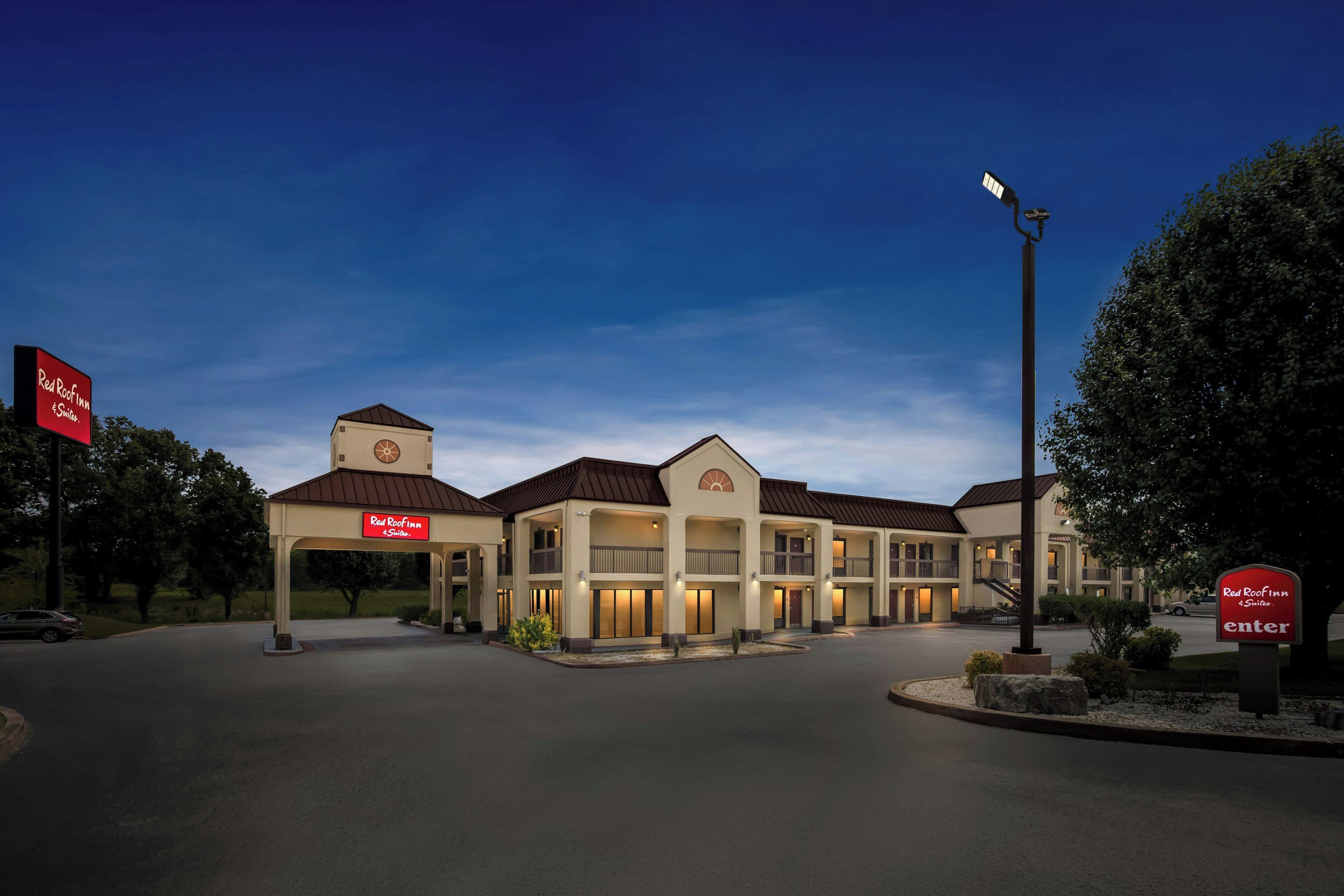 A Red Roof Inn with a central tower and multiple balconies, surrounded by trees and a clear sky.