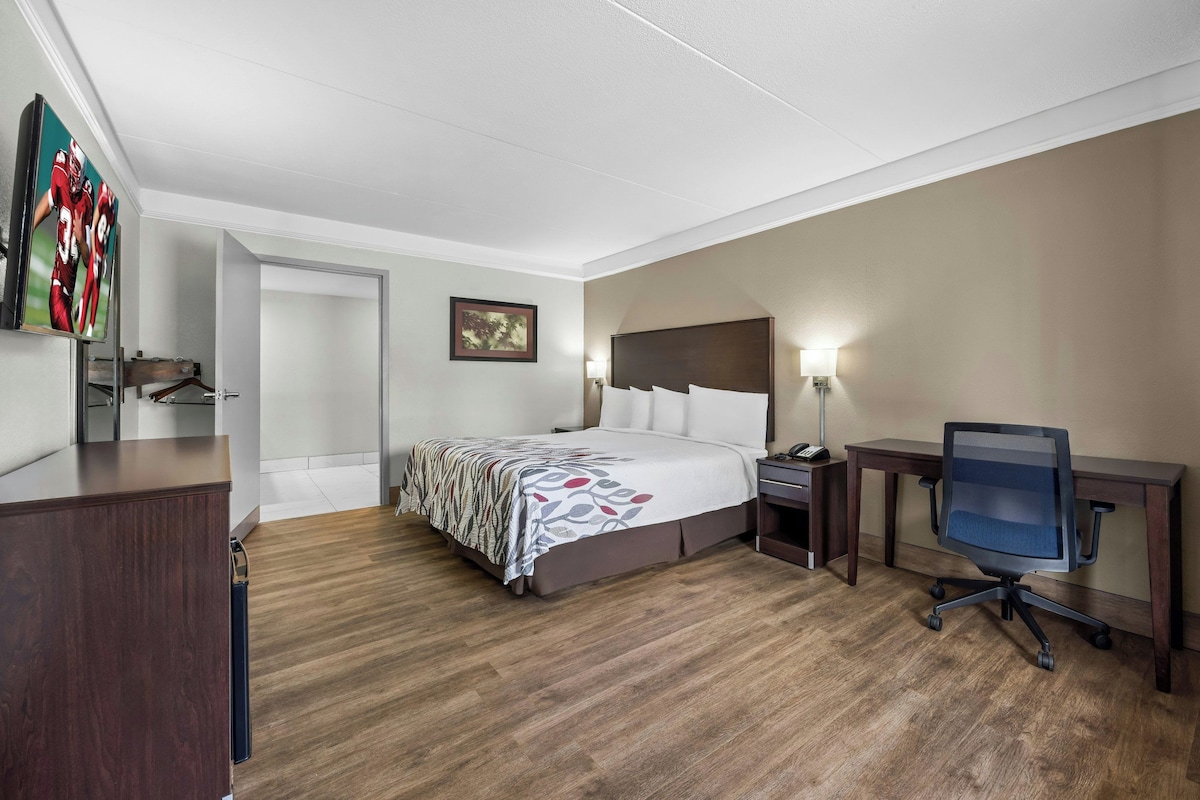 A hotel room with a bed, bedside table, desk, chair, and a wall-mounted TV.