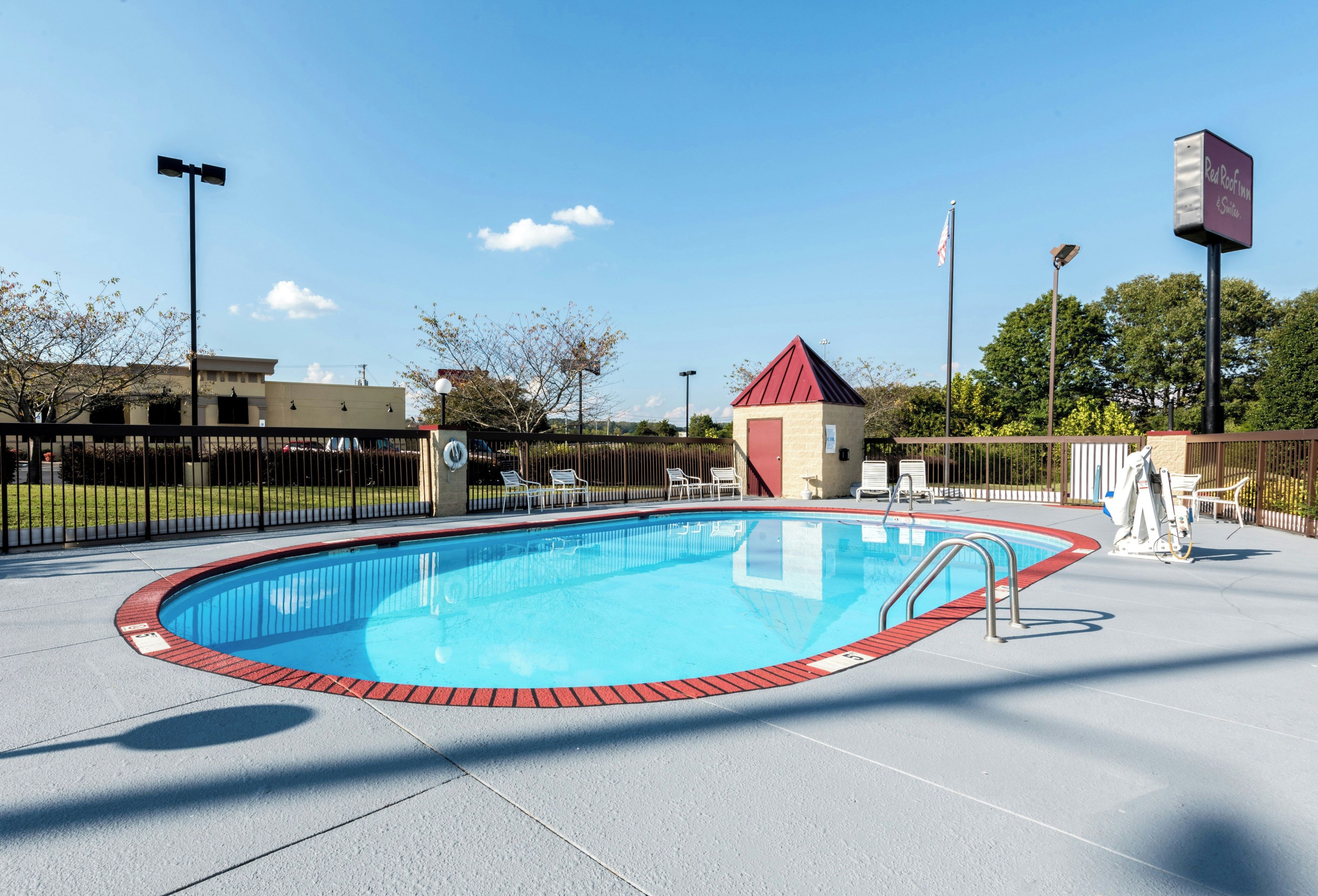 A clear blue pool with a red border, surrounded by a fence, and a small red-roofed building nearby.