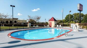 A clear blue pool with a red border, surrounded by a fence, and a small red-roofed building nearby.