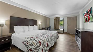 A hotel room with a large bed, a desk, a chair, a TV, and a wardrobe.