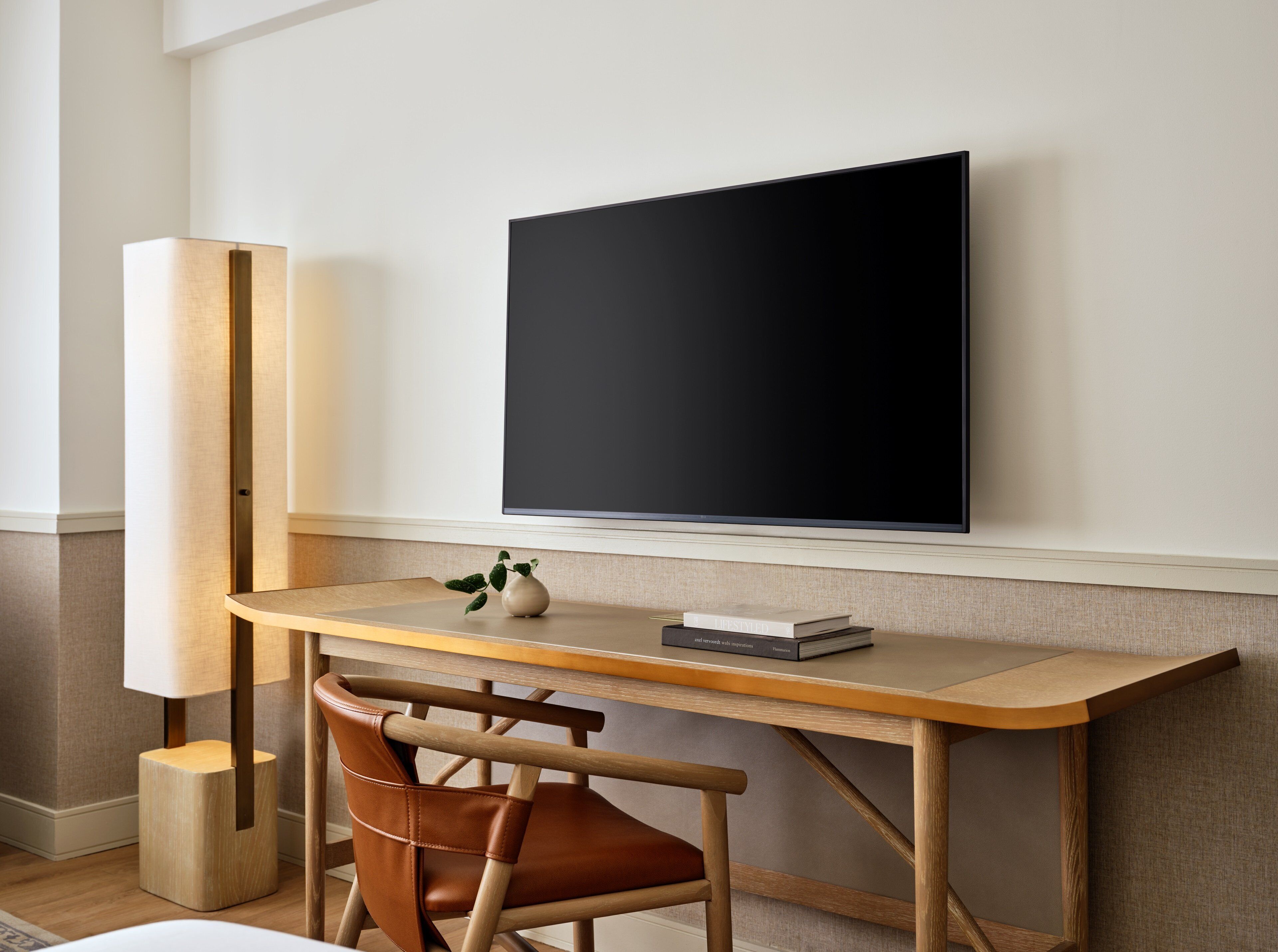 A modern room with a wooden desk, a chair, a television mounted on the wall, and a floor lamp.