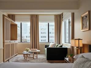 A hotel room with a bed, a green sofa, a small table with a vase, and a window with curtains. - Kimpton Ashbel New York Park Avenue (New York)