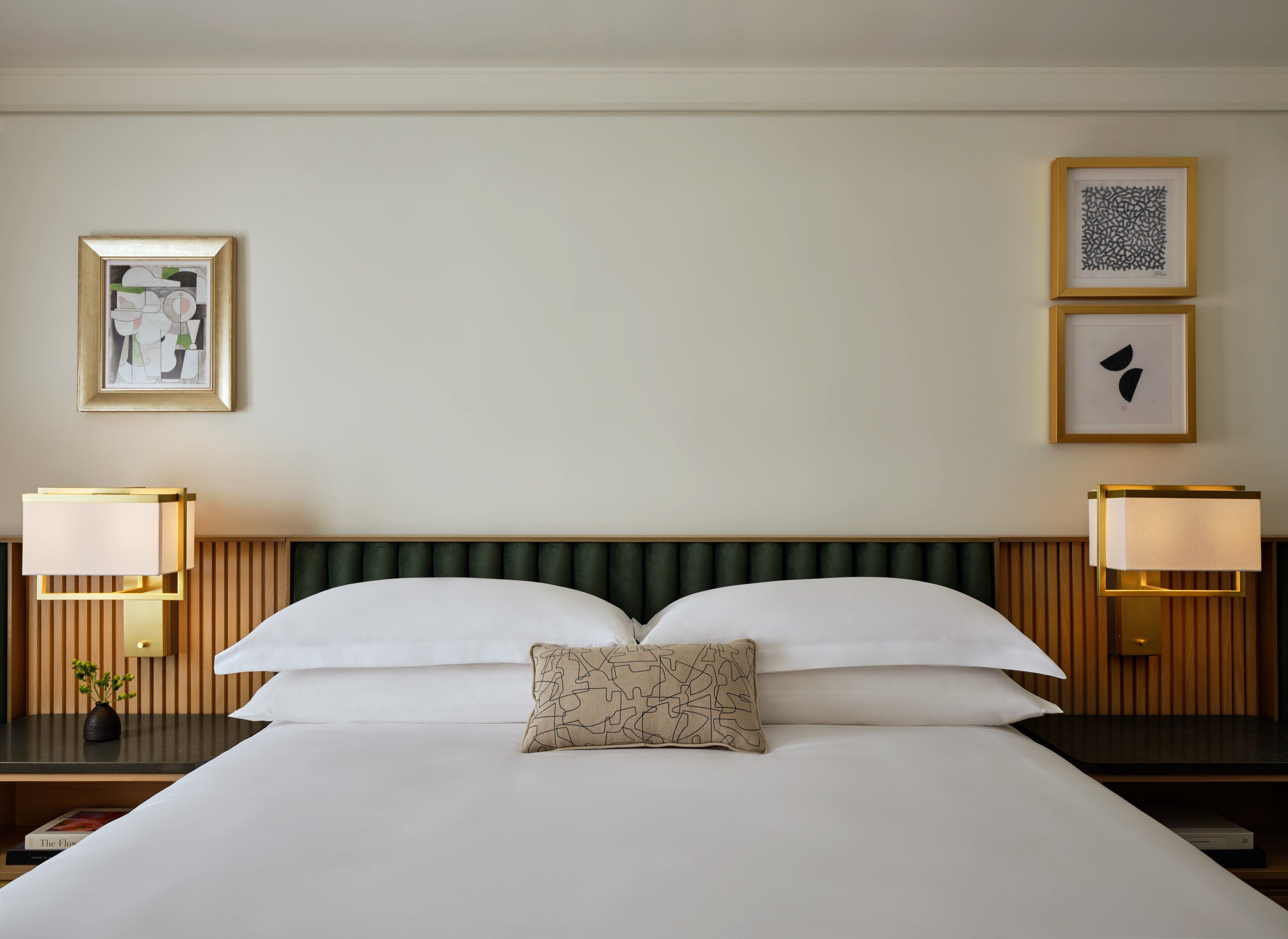 A hotel room with a large bed, two bedside lamps, a green upholstered headboard, and framed artwork on the walls.