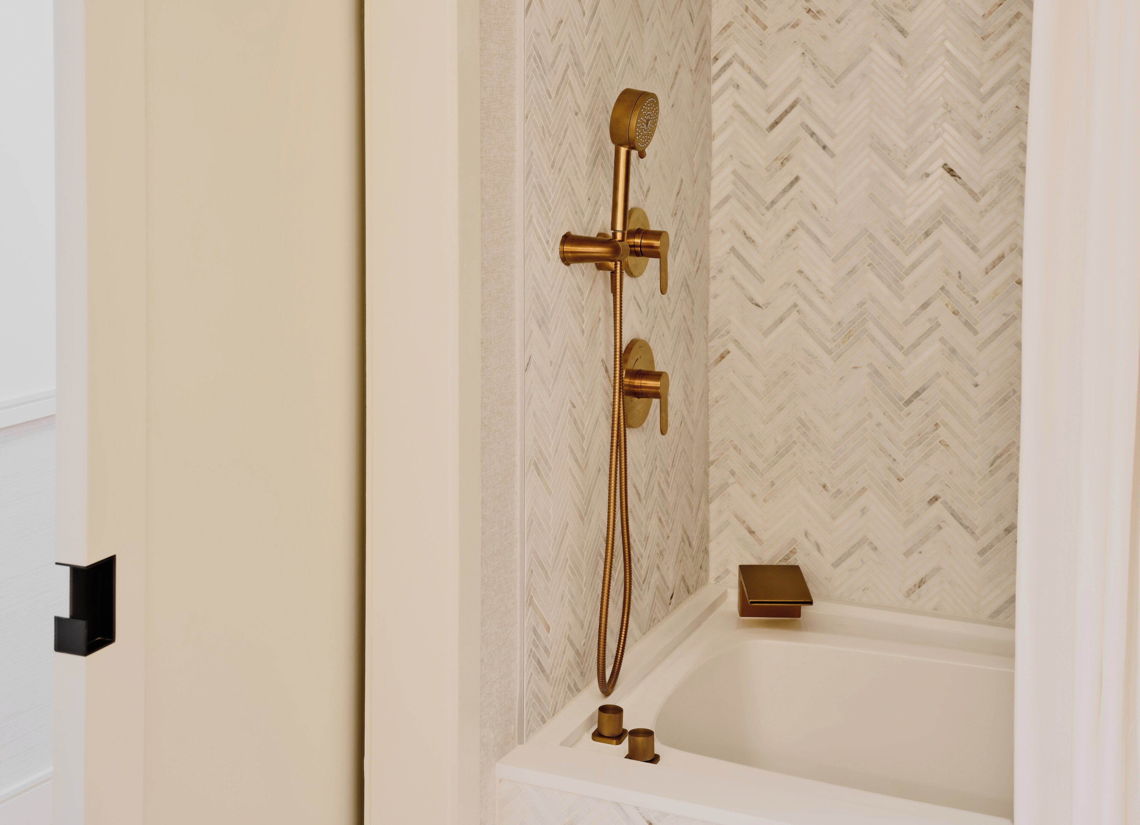 A bathroom with a herringbone patterned wall, a gold showerhead, and a white bathtub.