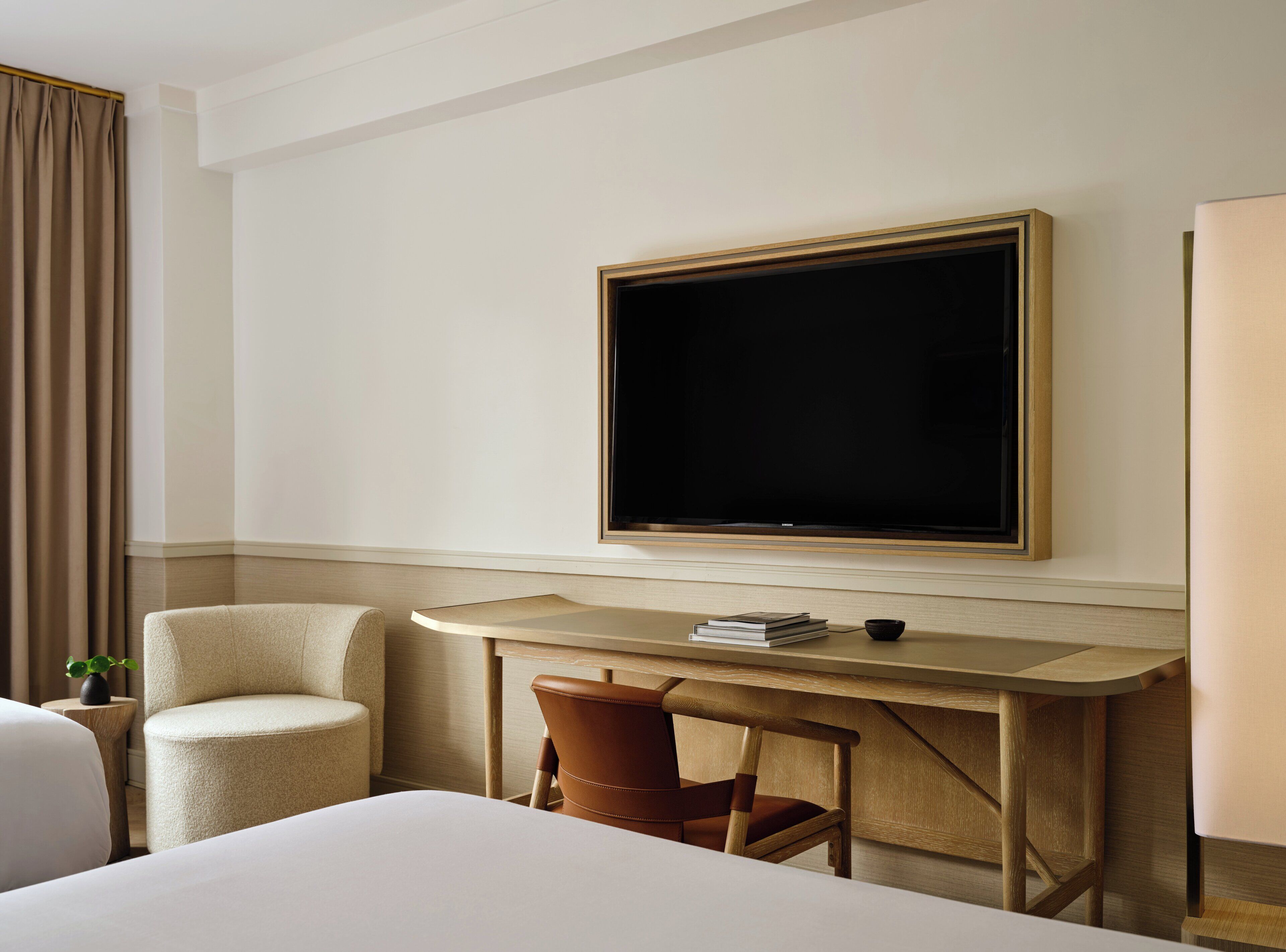 Ein Hotelzimmer mit einem Bett, einem Schreibtisch mit Stuhl, einem Fernseher und einem Fenster mit Vorhängen.