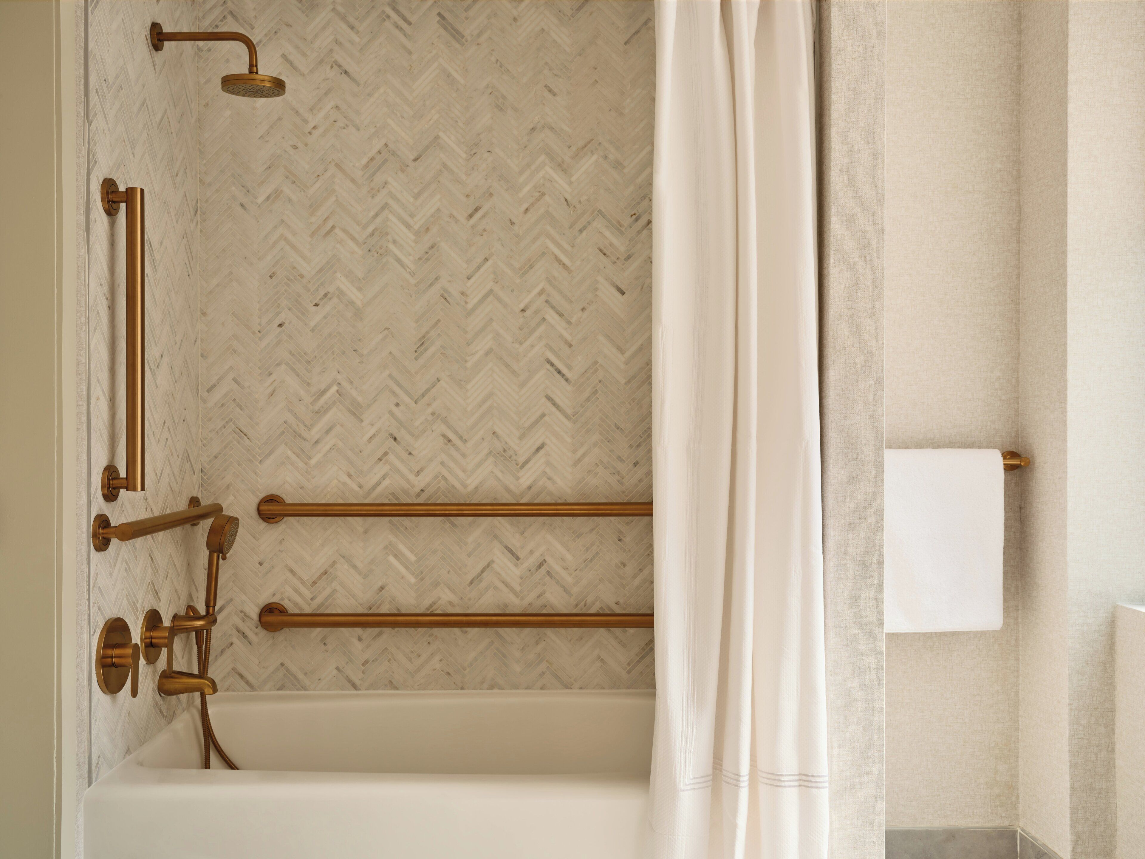 A bathroom with a herringbone patterned wall, a bathtub, a shower with a handheld showerhead, and a towel rack.