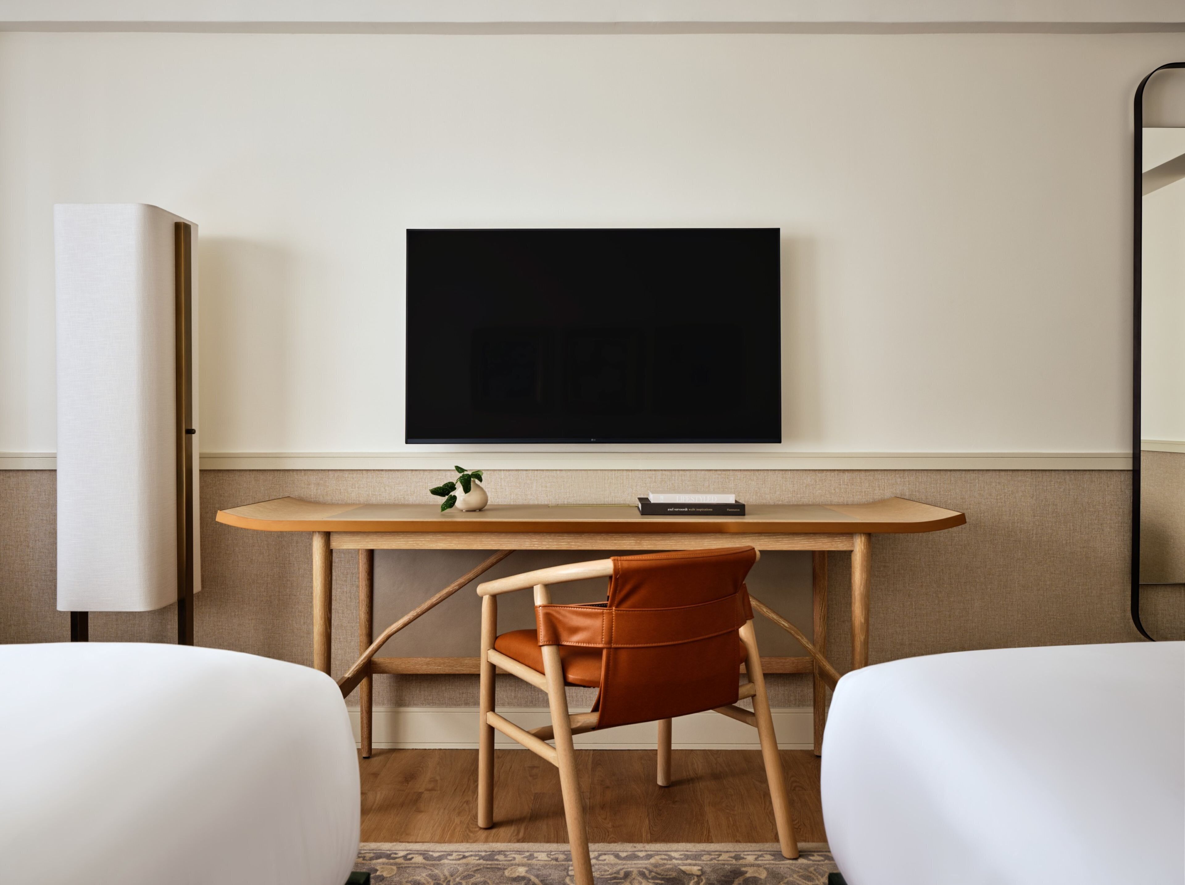 Una habitación de hotel con un escritorio de madera, un televisor montado en la pared y dos camas.