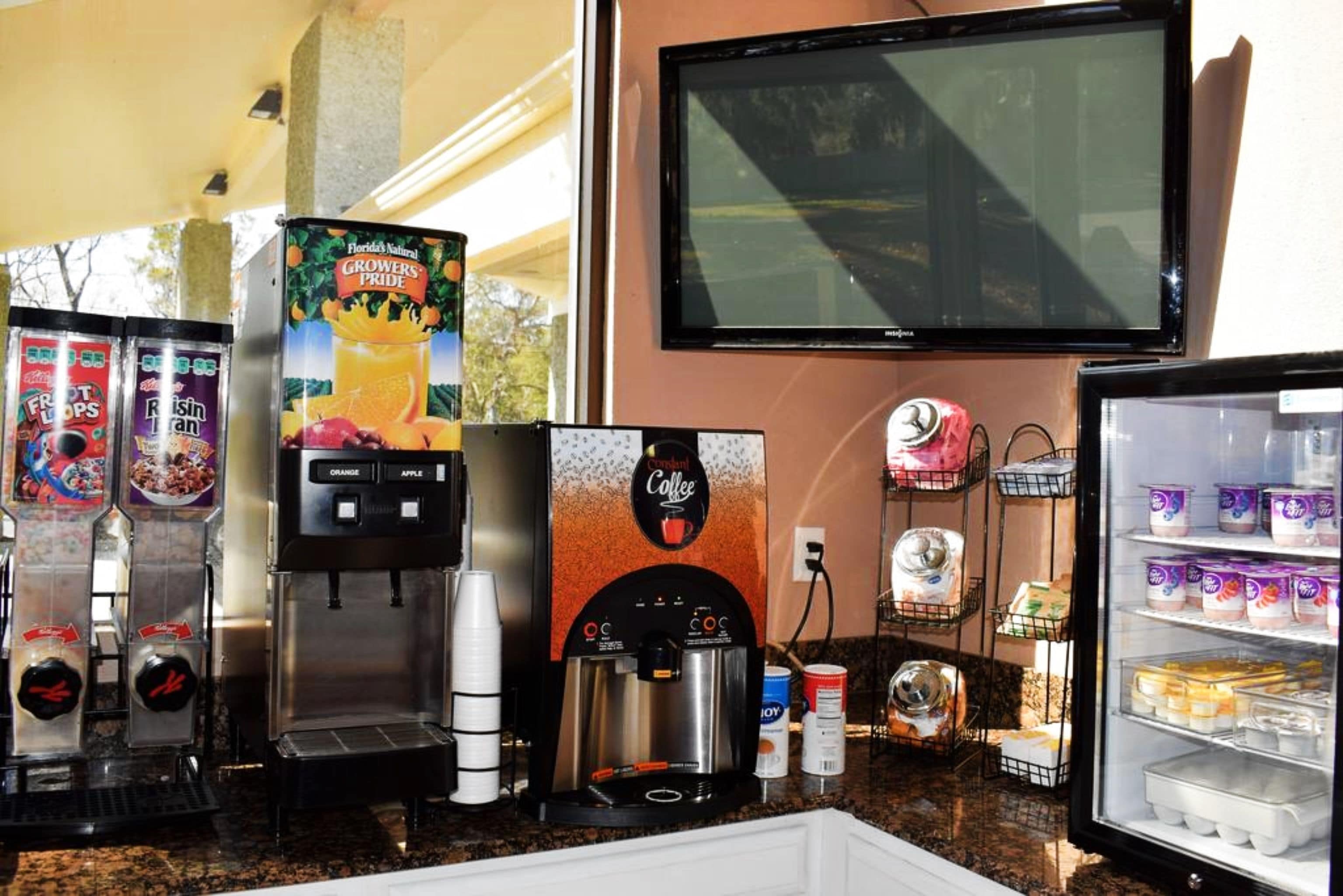 A coffee station with a coffee machine, a refrigerator stocked with yogurt, and a television mounted on the wall.