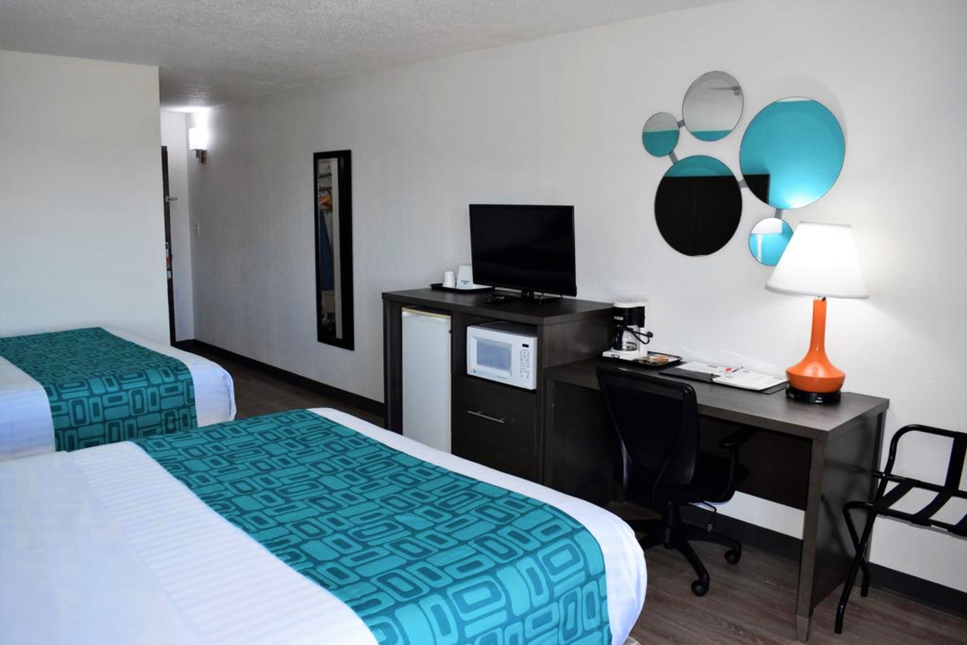 Een hotelkamer met twee bedden, een bureau met een computer, een televisie en een lamp.