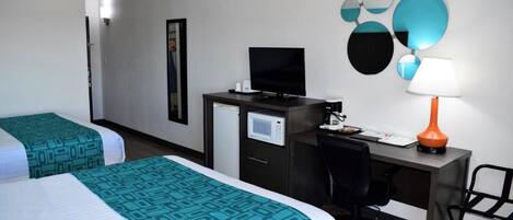 Habitación de hotel con dos camas, un escritorio con computadora, televisor y lámpara.